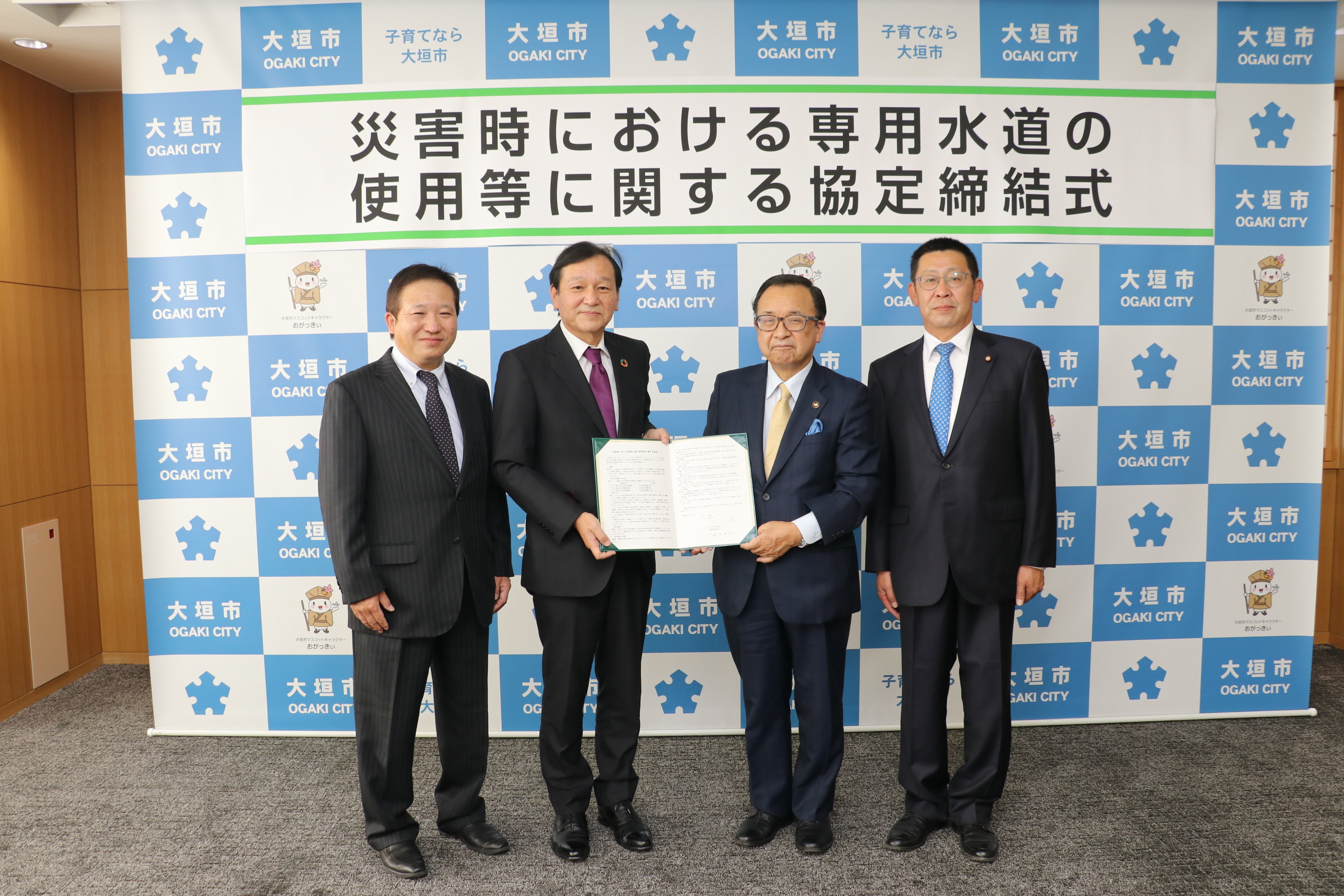 協定書を掲げる青木社長（左から2人目）と小川市長（右から2人目）